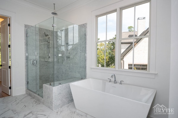 Large custom marble tile shower with glass enclosure and sculpted stand-alone tub