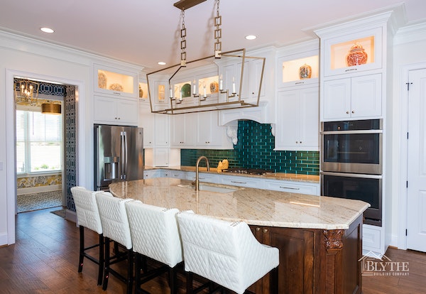 Luxury kitchen with white cabinets, green tile backsplash, and large pendant light