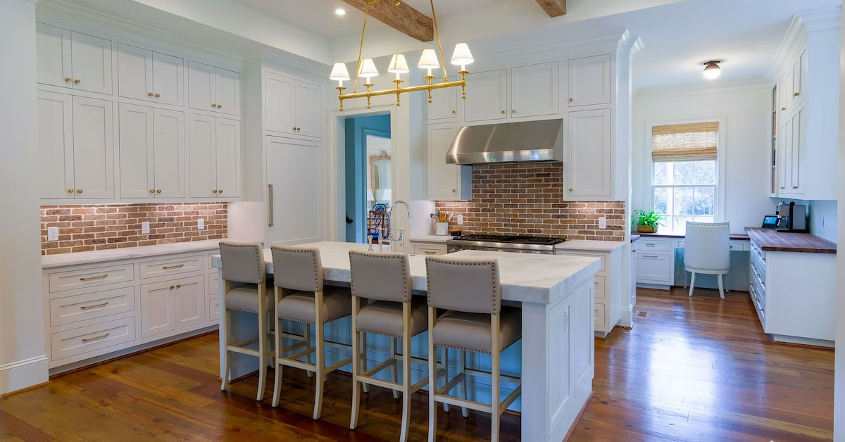 Modern Farmhouse-style kitchen with white Shaker cabinets, red brick backsplash, and large kitchen island with thick marble countertop.