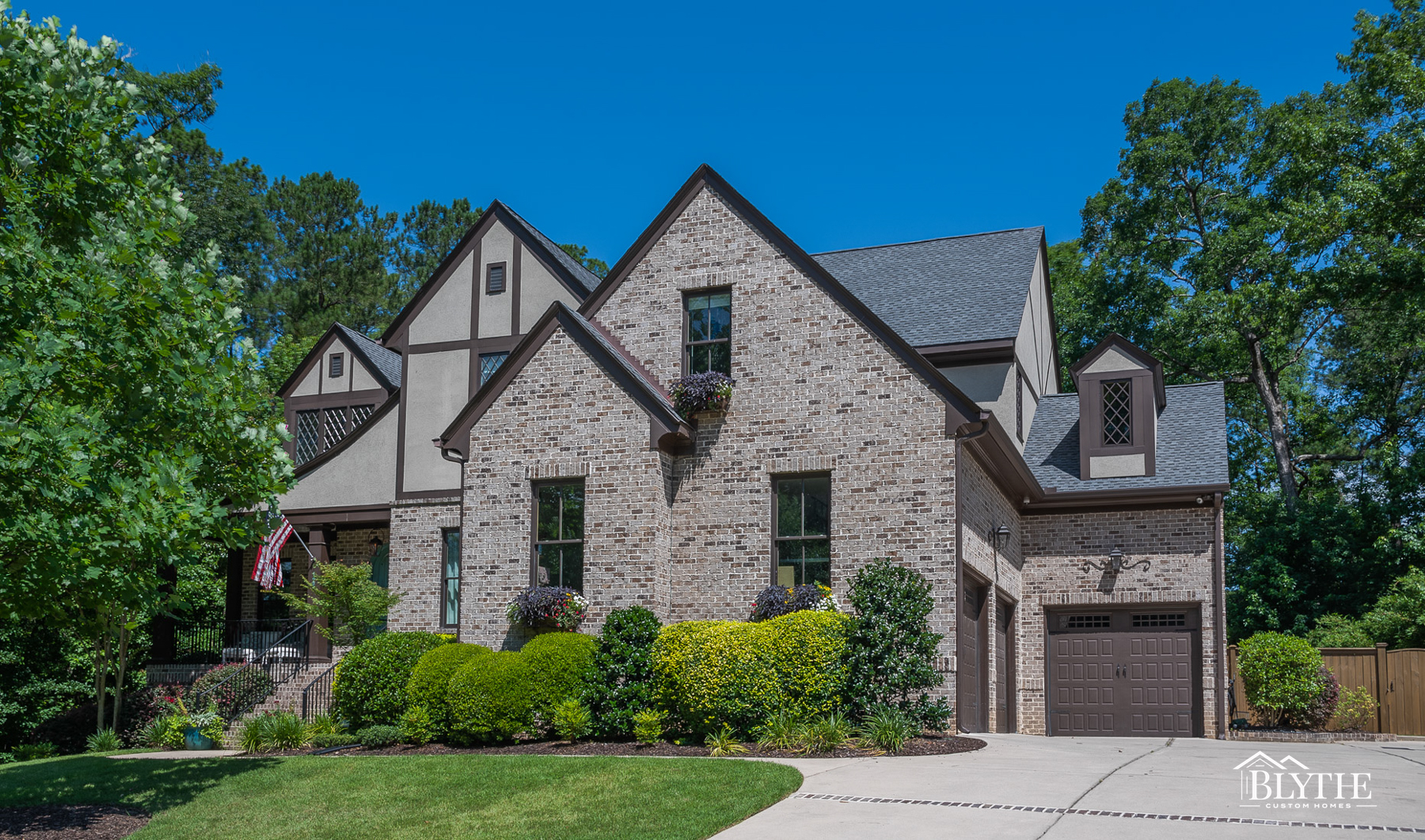 Brick and stucco Tudor-style home with 3-car garage, multiple front-facing gables, and beautiful shrubbery and front yard.