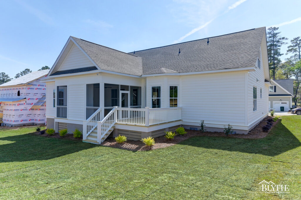 Rear of home with white Hardie board siding and a screened-in back porch with fireplace and adjoining deck and a flat backyard with new landscaping and sod.