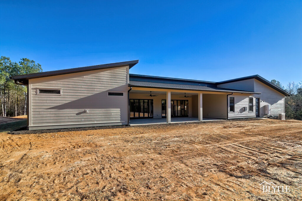 Rear exterior contemporary home with roof slanting up on each end and then a large covered porch in the middle and a back yard that's not sodded yet.