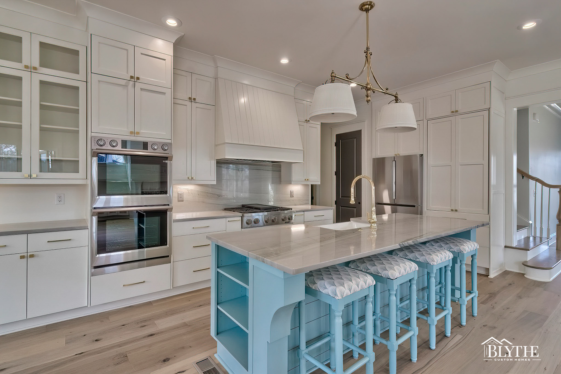 Powder blue kitchen island with four padded stools and kitchen with white floor-to-ceiling shaker cabinets and stainless steel appliances.