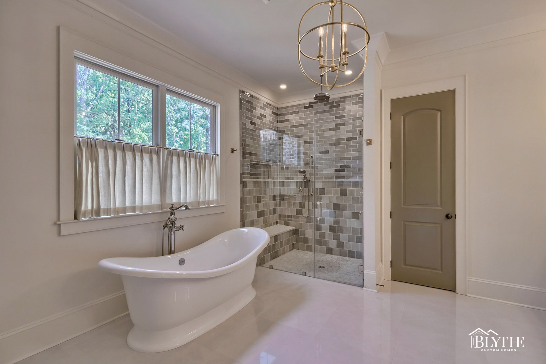 A large primary bathroom with separate white soaking tub and a large shower alcove with various shades of gray square and rectangular custom tiles.