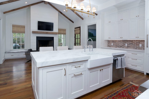 Kitchen with vaulted ceiling, white shaker cabinets, farmhouse sink, and brick backsplash