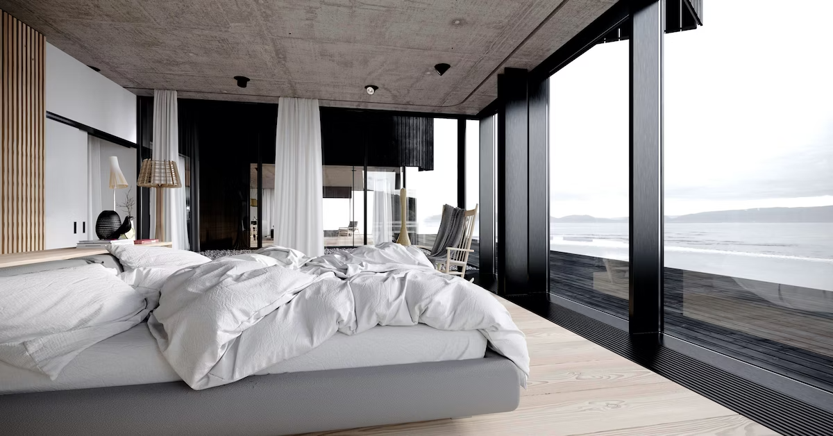 Modern luxury home bedroom with glass walls and ocean view and a king-sized bed with crumpled white comforter and white bedding.