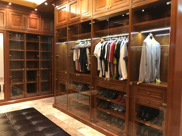 Hardwood and glass luxury closet with black cushioned ottoman and LED lighting