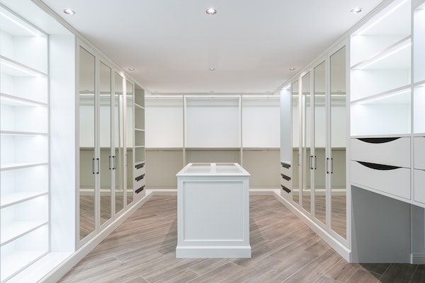 Luxury walk-in closet with closet island, white shelves, white drawers, and mirror closet doors