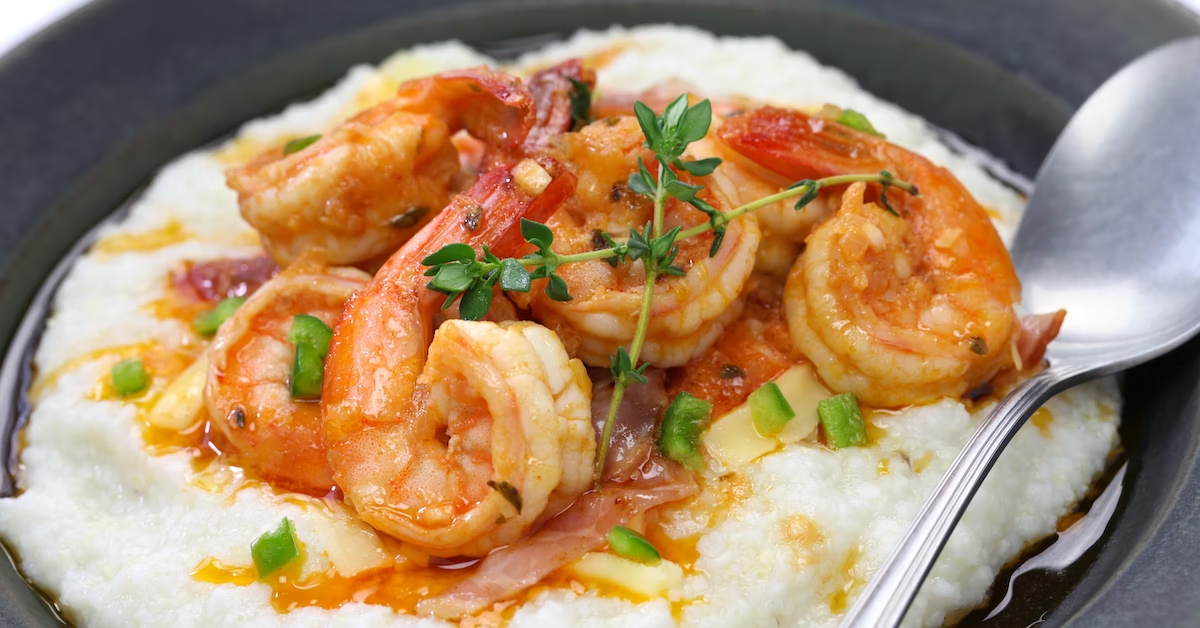 A closeup of shrimp and grits in a black bowl with a spoon.