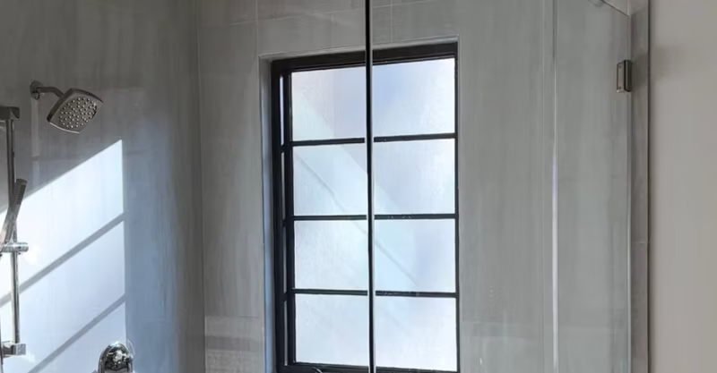An oversized custom-built steam shower with a frosted window, 2 shower heads, and glass surround.