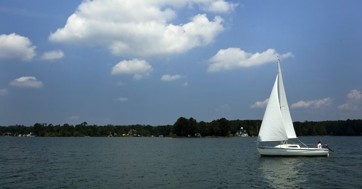 Lake Murray, South Carolina on a sunny day with a few clouds and a white sailboat with white sales in the middle of the water.