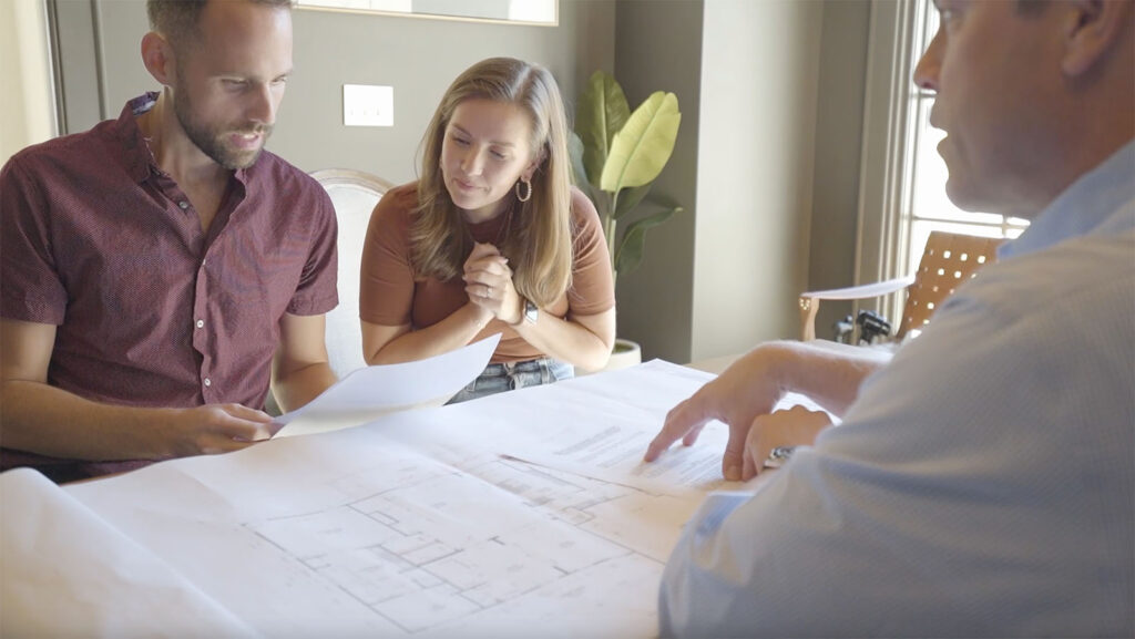 Lee Blythe in a blue shirt showing a couple their house plans over a table.
