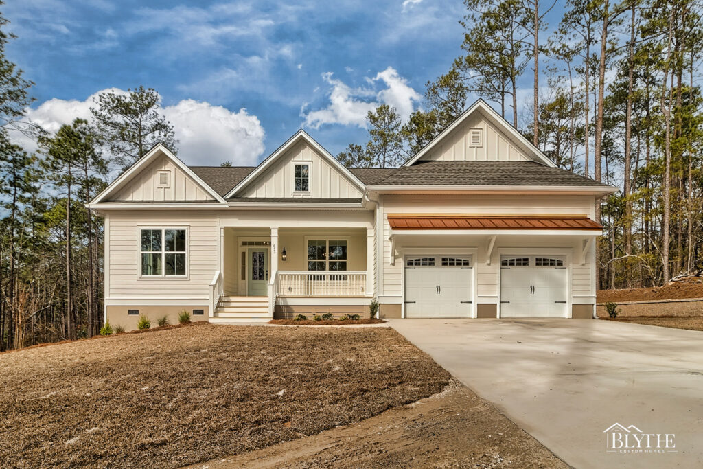 Front exterior of a Modern Craftsman/Modern Farmhouse home with Hardie siding, board and batten accents, 2 carriage garage doors, a front porch, 3 gables, and a copper metal roof accent over the garage.
