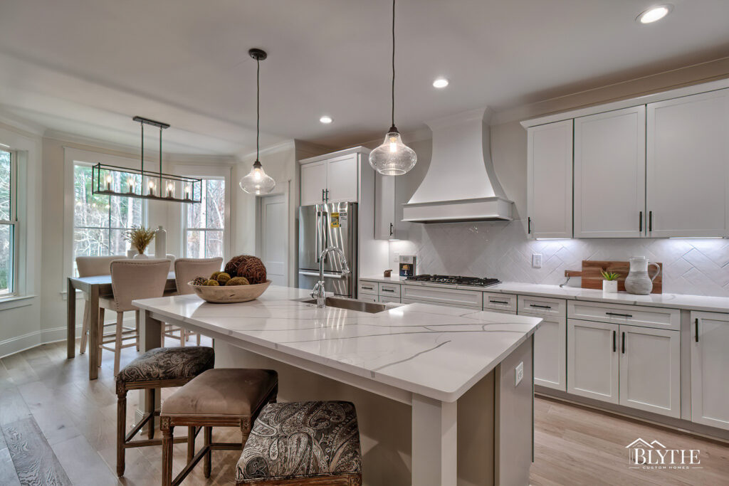 Gourmet kitchen with dramatic veined quartz countertops, two glass pendant lights over the island, a custom range hood cover, white Shaker cabinets, a herringbone white backsplash, and a breakfast nook