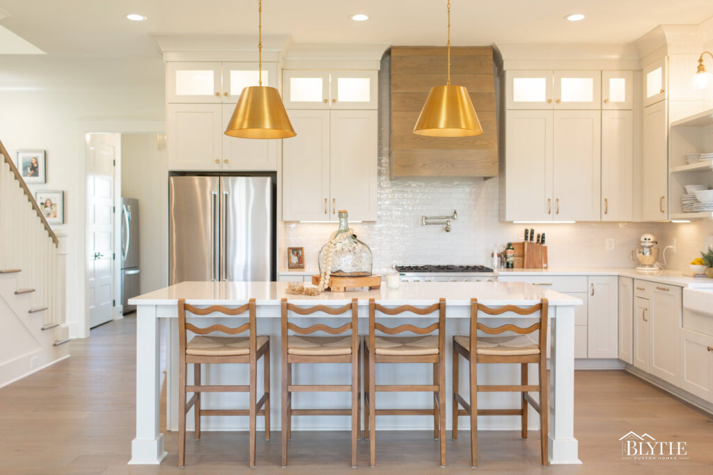 Modern farmhouse kitchen with white Shaker cabinets to the ceiling, a white island, 4 wood stools, light hardwood floors, and a white farmhouse sink.