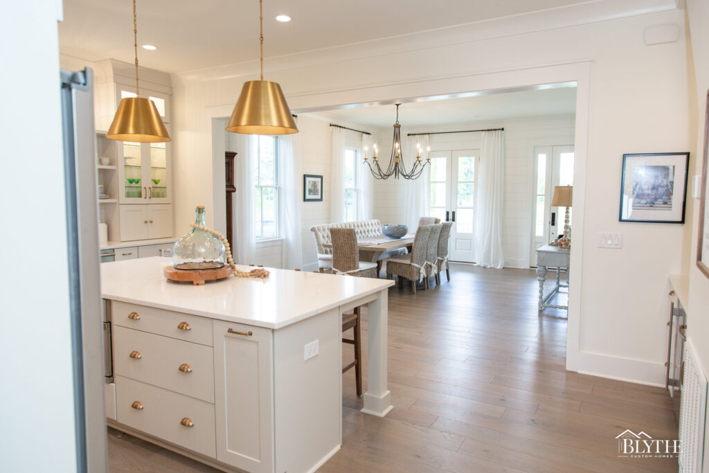 White kitchen island with gold pendant lights looking toward dining space in open-concept living area.