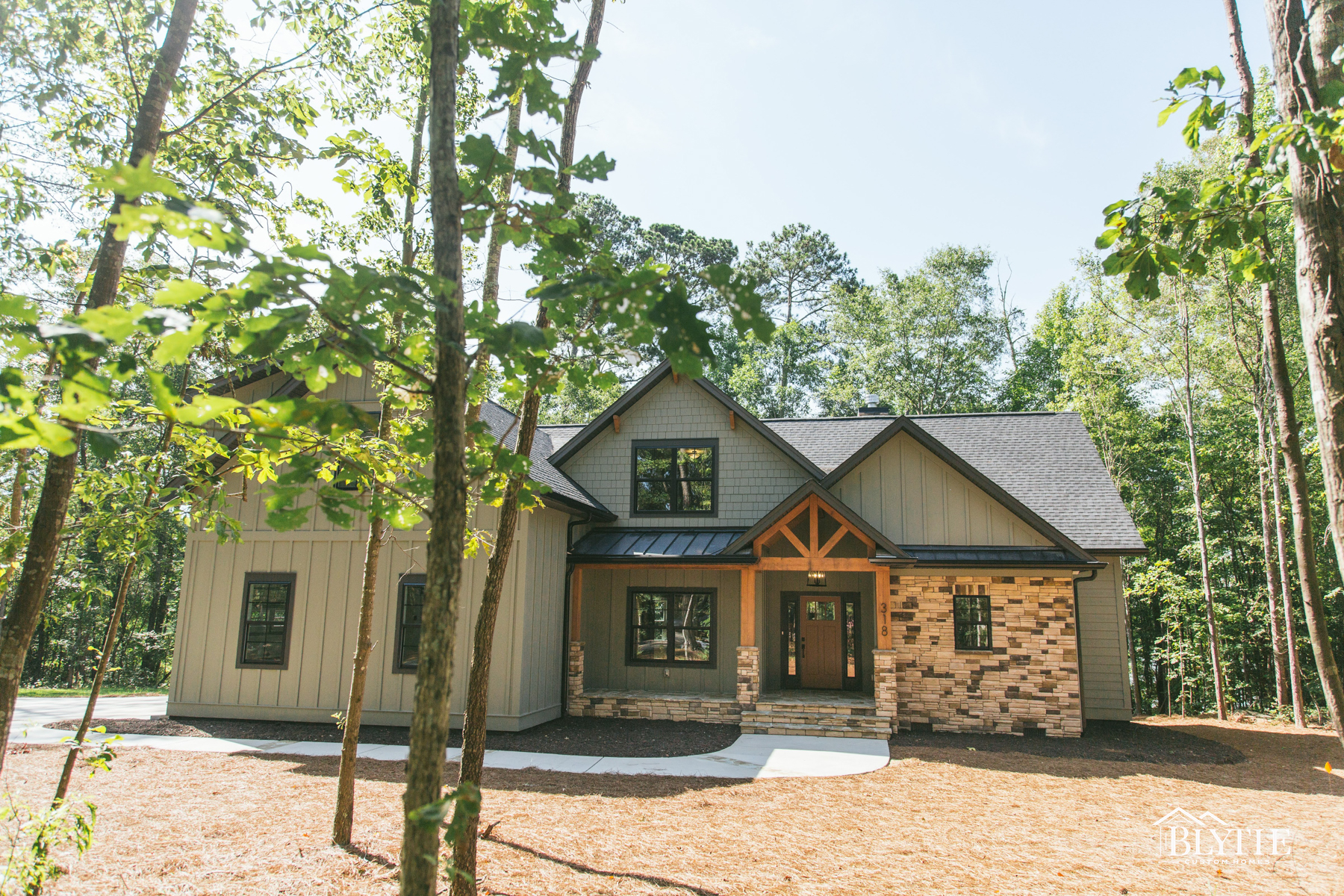 Front exterior of a eucalyptus green Modern Craftsman home with stone veneer, multiple gables, and a small front porch.