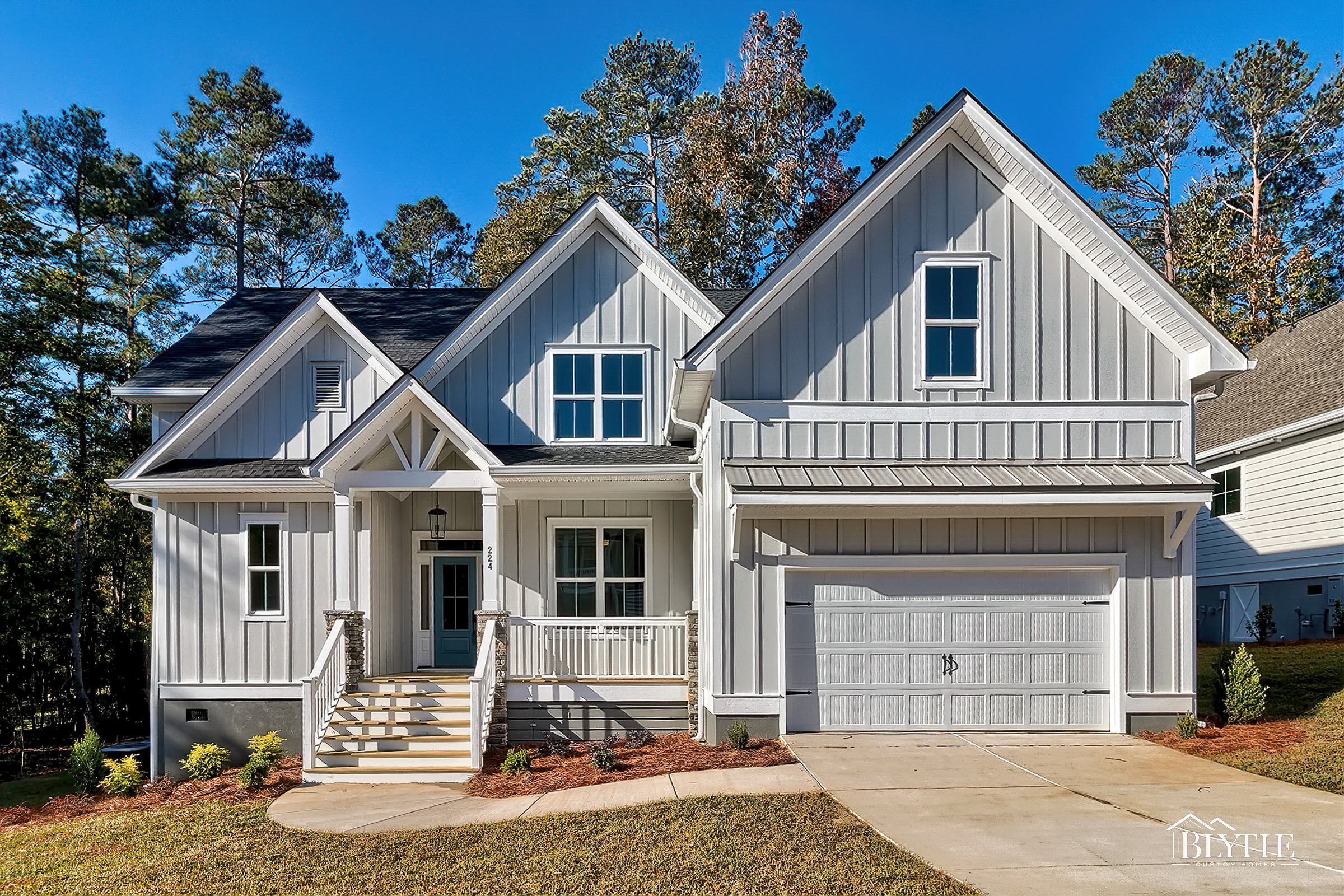 Front view of home with gray board and batten, multiple front-facing gables, white trim, craftsman details and front porch with stacked stone columns